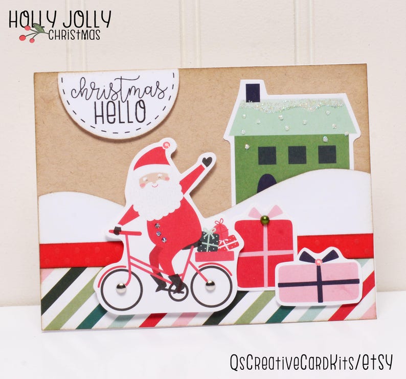 May include: A Christmas card with a red and white Santa Claus riding a bicycle with presents. The card has a green house with a white roof and the text "Christmas Hello" in a white circle.