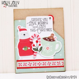 May include: A Christmas card with a polar bear wearing a red sweater and holding a cup of hot chocolate. The card also features a cup of hot chocolate with a gingerbread man and a candy cane. The text on the card reads "Sending you Love, Warmth and Cozy This Christmas".