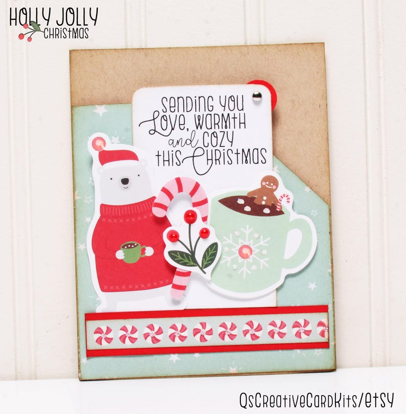 May include: A Christmas card with a polar bear wearing a red sweater and holding a cup of hot chocolate. The card also features a cup of hot chocolate with a gingerbread man and a candy cane. The text on the card reads "Sending you Love, Warmth and Cozy This Christmas".