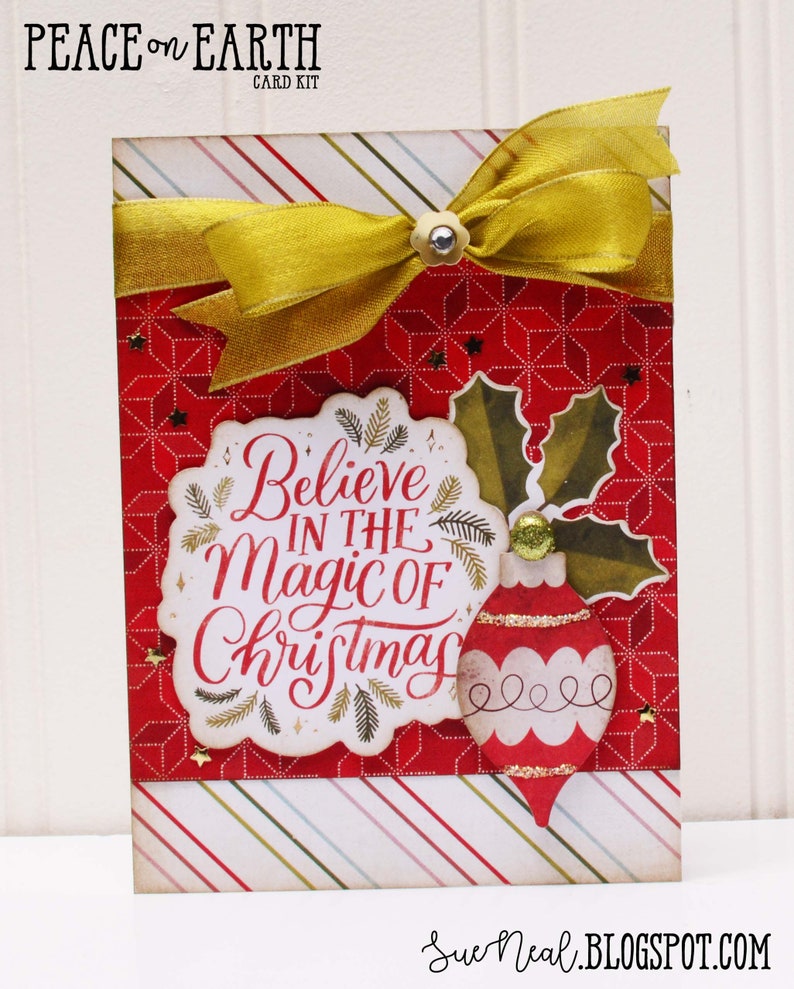 May include: A red and white Christmas card with a gold ribbon and a gold ornament. The card says "Believe in the Magic of Christmas".