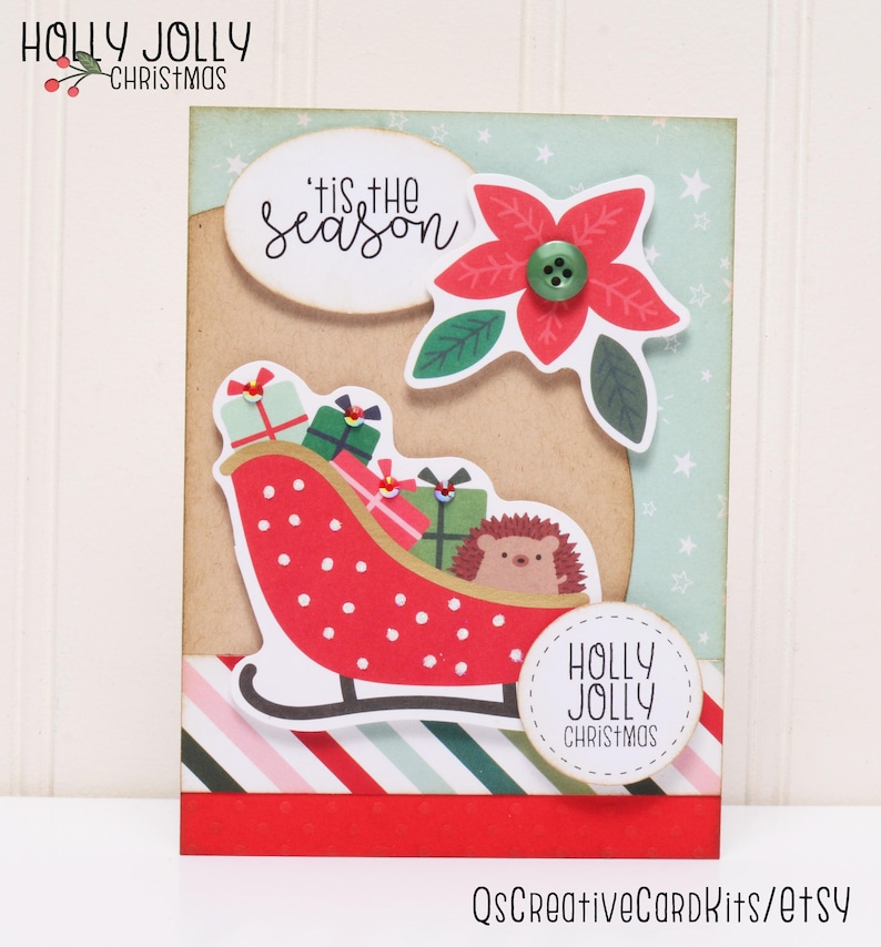 May include: A Christmas card with a red and white sleigh carrying presents and a hedgehog. The card has a green and white striped background with a red and white striped border. The card also has a red poinsettia flower with a green button in the center. The card says "'tis the season" and "Holly Jolly Christmas".