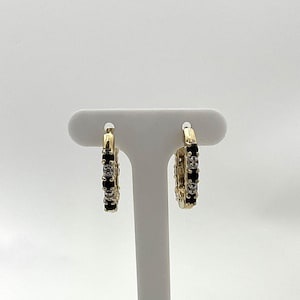 May include: A pair of gold hoop earrings with alternating black and clear gemstones. The earrings are displayed on a white jewelry stand against a white background. The gemstones are small and evenly spaced around the hoops.
