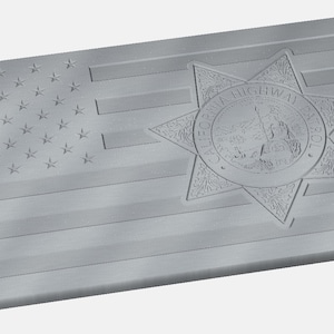 Op de afbeelding: Een grijze metalen plaquette met een gegraveerde Amerikaanse vlag en een ster van de California Highway Patrol. De ster heeft de woorden "California Highway Patrol" rond de rand.