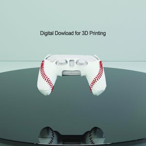 Peut inclure: Manette de jeu vidéo blanche avec des coutures rouges, ressemblant à un ballon de baseball. Le texte "Téléchargement numérique pour l'impression 3D" est au-dessus de la manette.