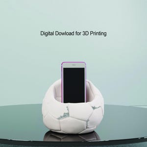 May include: White 3D printed phone stand shaped like a soccer ball. The stand has a small indentation to hold a phone.  Digital Dowload for 3D Printing.
