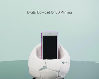 Op de afbeelding: Witte 3D-geprinte telefoonstandaard in de vorm van een voetbal. De standaard heeft een kleine inkeping om een telefoon vast te houden. Digitaal downloaden voor 3D-printen.