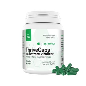 May include: A green plastic bottle with a white lid labeled "ThriveCaps substrate vitalizer" with the text "Macros | Micros | Essential Minerals" and "Contains 60 caps". The bottle is sitting on a white surface with a pile of green capsules in front of it.