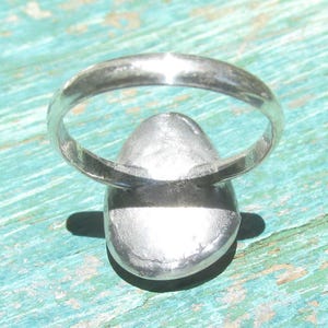 May include: A silver-toned ring featuring a smooth, rounded, metallic setting. The band is thin and circular, connecting to a solid, slightly domed, oval-shaped centerpiece. The metal surface has a reflective, polished finish throughout the entire piece.