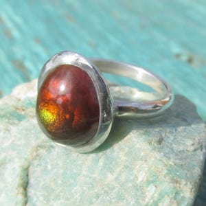 Puede incluir: Un anillo de plata con una gema grande de forma ovalada. La gema es de color marr&oacute;n rojizo intenso con destellos iridiscentes amarillos y verdes. El anillo tiene una banda de plata pulida y sencilla. La gema mide unos 2 cm.