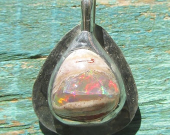May include: A teardrop-shaped pendant featuring a polished opal gemstone with vibrant red, green, and orange flashes of color set within a smooth, dark silver-toned metal frame that includes a sturdy bail at the top for hanging on a chain.