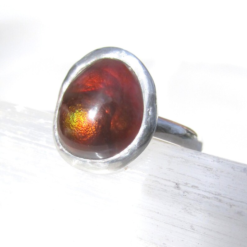 Puede incluir: Un anillo de plata con una gema ovalada grande. La gema es de color marr&oacute;n rojizo intenso con destellos iridiscentes dorados y verdes. El anillo tiene una banda de plata pulida simple. La gema mide unos 2,5 cm de largo.