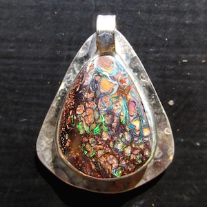 May include: A silver pendant with a triangular frame. The pendant features a colorful opal stone with a mix of brown, orange, green, blue, and purple hues. The stone is set within a silver bezel.