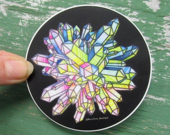 May include: A circular sticker featuring a vibrant illustration of a crystal cluster with multifaceted points in shades of neon yellow, bright blue, magenta, and soft pink against a solid black background, with the text @MoonTree_Boutique.