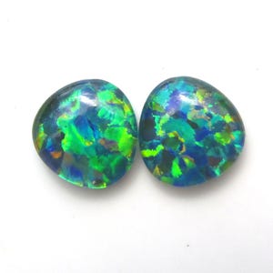 Puede incluir: Dos ópalos ovalados con un vibrante juego de colores. Las piedras preciosas muestran una mezcla de azules, verdes y toques de amarillo, creando un efecto brillante. Los ópalos están sobre un fondo blanco.