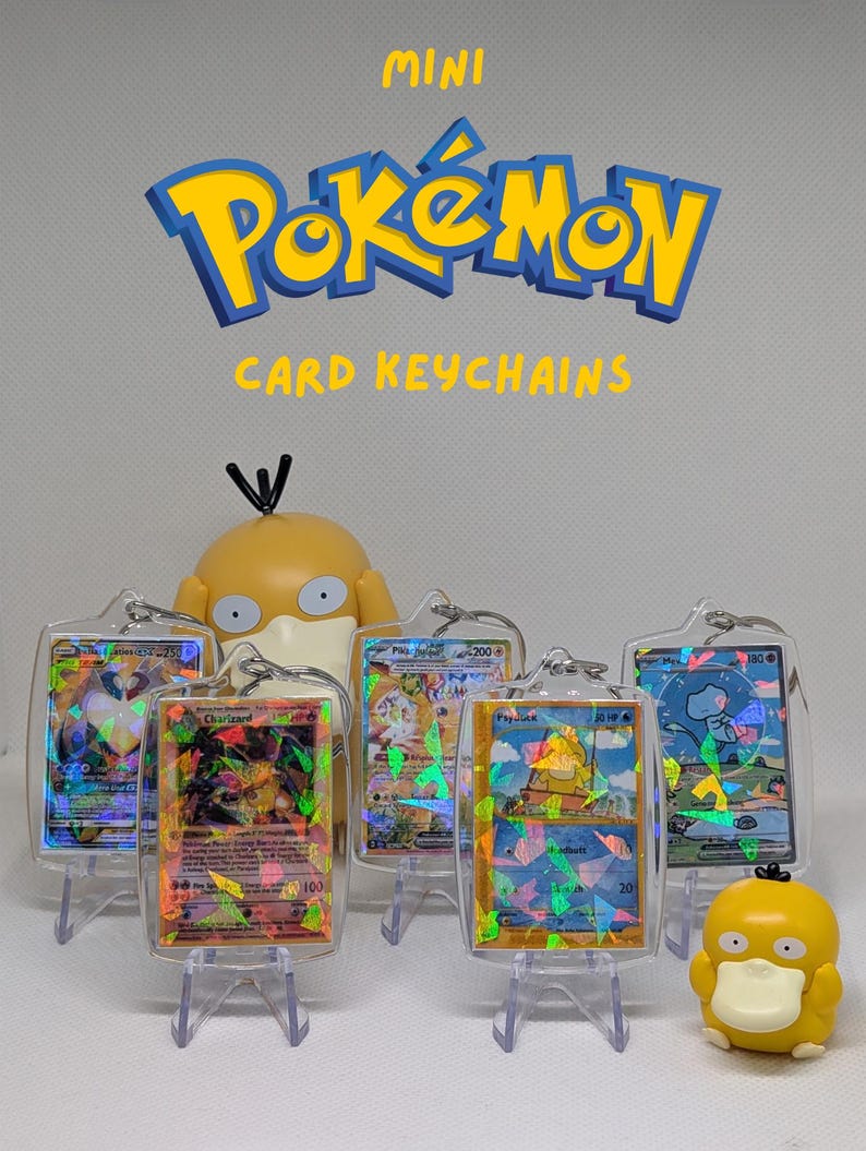 May include: Five mini Pok&eacute;mon card keychains in clear protective cases, each featuring a holographic trading card. The text MINI POK&Eacute;MON CARD KEYCHAINS is displayed above. Two yellow Psyduck figurines are positioned among the keychains.