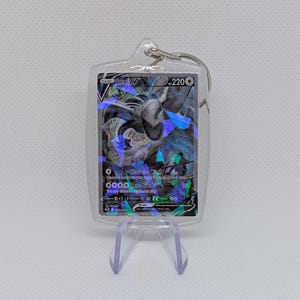 May include: A clear acrylic keychain containing a Lugia V trading card with 220 HP. The card features a holographic finish with blue and purple geometric shards, displaying the text Lugia V, 220, Read the Wind, and Aero Dive.
