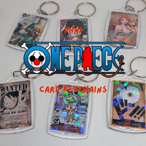 May include: Six rectangular clear acrylic keychains featuring One Piece trading cards with holographic foil details. The cards display various anime characters and the text MINI ONE PIECE CARD KEYCHAINS. Each keychain has a silver metal ring.