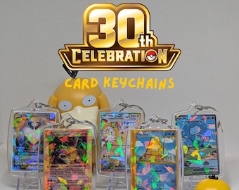 May include: A collection of mini Pokémon Trading Card Game 30th Celebration card keychains featuring holographic cards encased in clear plastic protectors. The display includes a yellow Psyduck figure and various character cards with colorful foil accents.