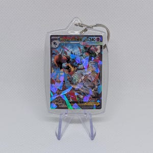 May include: A clear acrylic keychain featuring a Mega Lucario EX trading card with a holographic shattered glass finish. The card displays the character Lucario, the text Mega Lucario EX, and a health value of 340. A metal ring is attached to the top.