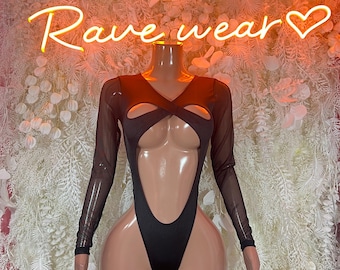 May include: Black bodysuit with long sheer sleeves and cut-out details. The garment is displayed on a mannequin against a backdrop with the neon sign that reads "PURR Rave wear". The bodysuit has a V-neckline and a high-cut leg.