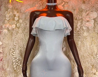 May include: A light blue strapless mini dress featuring a ruffled neckline overlay and a matching choker with a small central embellishment. The garment is displayed on a dark mannequin against a backdrop with neon text reading Rave wear.
