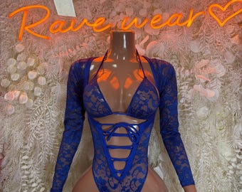 May include: A blue lace bodysuit with long sleeves and a halter top. The bodysuit features a lace-up front and a floral pattern. The mannequin is displayed in front of a white floral background. The neon sign says "Rave wear".