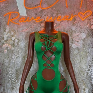 May include: A bright green bodysuit with cut-out details and lace-up accents. The sleeveless garment features a high neckline and shorts-style bottom. The words "Rave wear" are visible in neon orange in the background.