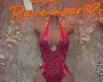 May include: A one-piece bodysuit featuring a vibrant neon pink and black leopard print pattern. The garment has a deep plunging neckline, a halter-style strap, and side cutouts accented with thin pink lace-up ties along the torso and hips.