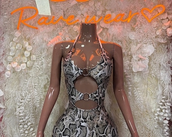 May include: A sleeveless mini dress featuring a snakeskin print in shades of gray, black, and tan. The garment has a halter neckline, two circular silver-toned metal rings at the center chest and waist, and two cutouts on the front torso.