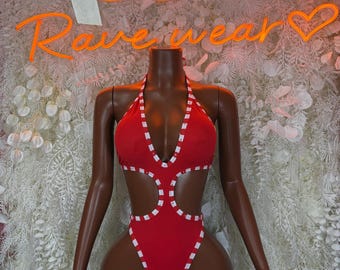 May include: A red halter-neck swimsuit with white stitched detailing. The one-piece suit features cut-out sections and a high-cut leg. The mannequin is set against a backdrop with the neon text "Rave wear".