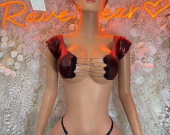 May include: A mannequin wearing a burgundy two-piece outfit. The top is a short-sleeved crop top with a lace-up design. The bottom is a thong with gold ring accents. The background features a neon sign that says "Rave Ear".