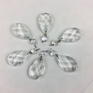 May include: Six clear glass teardrop-shaped crystal prisms with metal loops for hanging.