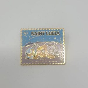 May include: A gold-colored pin shaped like a postage stamp with a blue background and a cartoon image of Pluto the dog wearing a space suit and holding a globe. The text "5c SAINT LUCIA" is printed on the stamp. The text "10th anniversary of moonwalk" is printed at the bottom of the stamp.