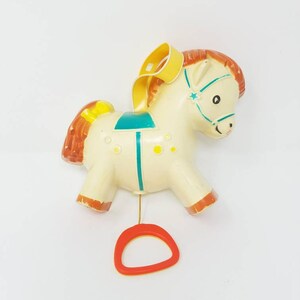 Puede incluir: Un caballo de juguete vintage de cuerda con una cuerda de tiro amarilla. El caballo es blanco con detalles marrones y amarillos y detalles azules y verdes. El caballo tiene una estrella en la frente y una silla de montar amarilla.