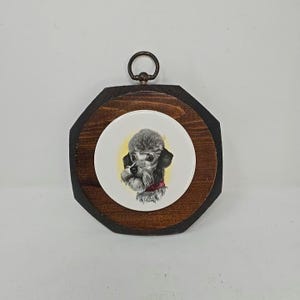 May include: A vintage wall hanging featuring a poodle portrait. The artwork is set within a dark brown, octagonal wooden frame. The poodle is depicted in black and white with a red collar, set against a yellow background.