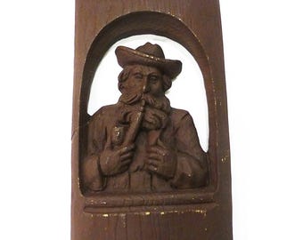 Figura tallada en madera de un hombre fumando en pipa de material desconocido