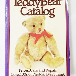 Könnte beinhalten: Der Einband des Buches "The Teddy Bear Catalog" zeigt einen Teddybären im Vintage-Stil mit einem roten Band. Der Titel des Buches lautet "The Teddy Bear Catalog" und der Untertitel lautet "Prices, Care and Repair, Lore, 100s of Photos. Everything. Peggy & Alan Bialosky".