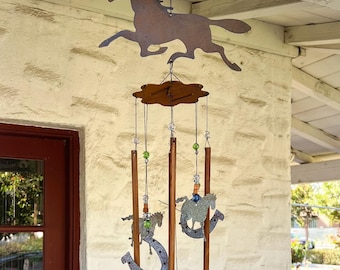 May include: A rustic metal wind chime featuring horse silhouettes and a horseshoe. The wind chime has wooden rods, decorative beads, and a running horse silhouette at the top. The bottom of the chime has a horse silhouette.