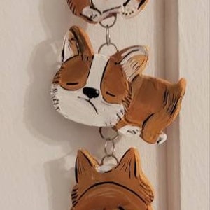 May include: A string of five ceramic dog ornaments, each painted with a different expression. The ornaments are connected by a silver chain and a bone charm hangs at the bottom.