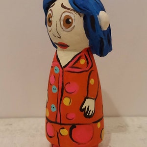 Puede incluir: Mu&ntilde;eca de madera pintada a mano con cabello azul, un vestido de lunares rojos, rosas y amarillos y una cara blanca con ojos marrones.
