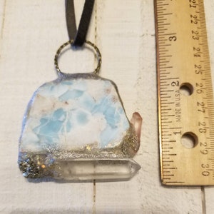 May include: A blue and white agate pendant with a clear quartz point, set in a silver-colored metal frame with a gold-colored chain. The pendant is approximately 2 inches in length.