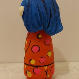 Puede incluir: Una mu&ntilde;eca de madera pintada a mano con cabello azul y un vestido rojo con lunares rosas y amarillos.