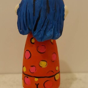 Puede incluir: Una mu&ntilde;eca pintada a mano con cabello azul y un vestido rojo con lunares rosas y amarillos.