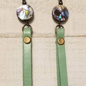 May include: A pair of dangle earrings with a green leather tassel and a round iridescent abalone shell charm.