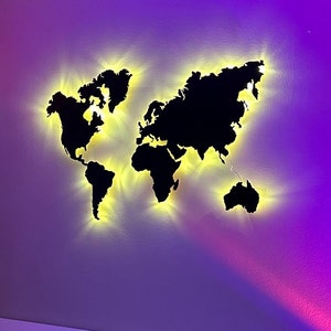 Puede incluir: Un dormitorio con una cabecera blanca y una silueta de mapa del mundo negro con luces amarillas en la pared. La habitación está iluminada con luces moradas y rosadas. Hay una mesita de noche blanca con una lámpara blanca y una taza con el texto "No seas blando, toma café" en ella.