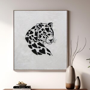 Puede incluir: Una ilustración en blanco y negro de un leopardo en una impresión de lienzo blanco. La impresión está enmarcada y colgada en una pared sobre un gabinete de madera.