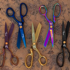 May include: Five pairs of Cut Sharp scissors in various finishes: one purple, one blue, one gold, one iridescent rainbow, and one matte black. Each pair features a central gold-toned screw and the Cut Sharp logo printed on the blade and handle.