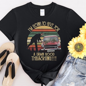 Puede incluir: Camiseta negra con un gráfico de estilo vintage que muestra a un hombre en un coche con el texto "I'm going to give you a damn good thrashing!!"