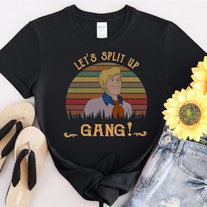 以下が含まれることがあります： 「Let's Split Up Gang!」というテキストと、漫画のキャラクターのヴィンテージスタイルのグラフィックが描かれた黒いTシャツ