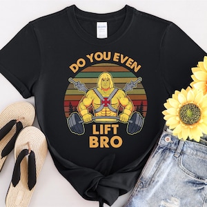 May include: Black t-shirt featuring a retro-style graphic of He-Man lifting weights. The text "Do you even lift bro" is printed on the shirt.